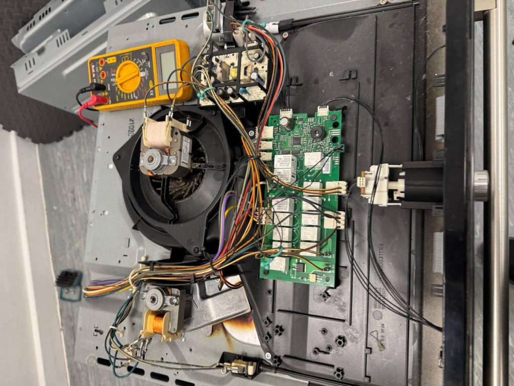 Built-in electric oven with the casing off, showing the control board, fan motor and wiring