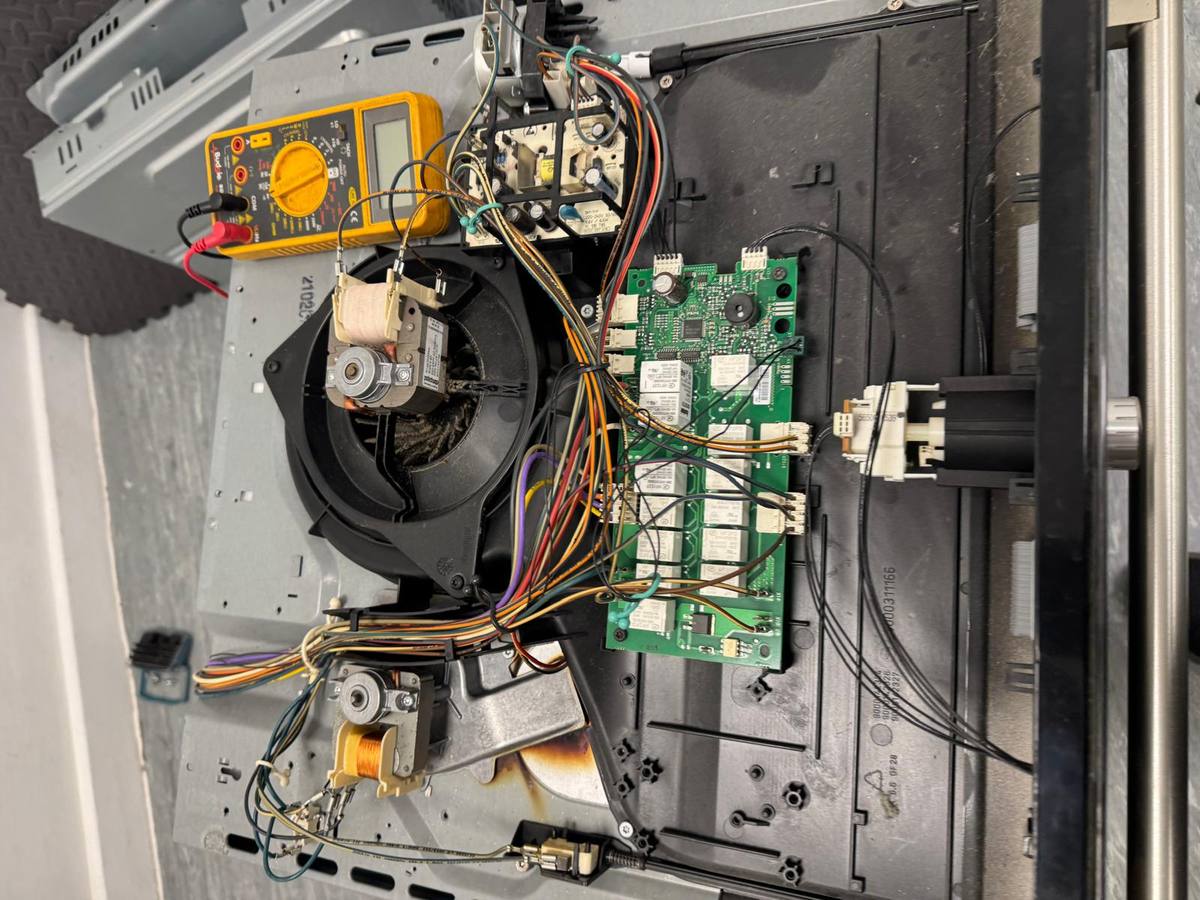 Built-in electric oven with the casing off, showing the control board, fan motor and wiring
